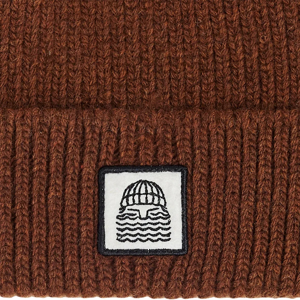 Gros plan sur l’écusson surfwear noir et blanc cousu sur le revers du bonnet To the Sea marron