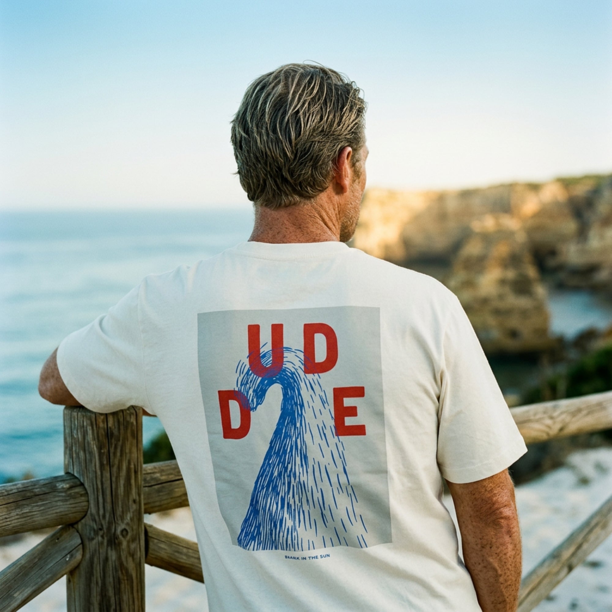 tee shirt blanc avec vague stylisée dans le dos porté par homme sur une plage