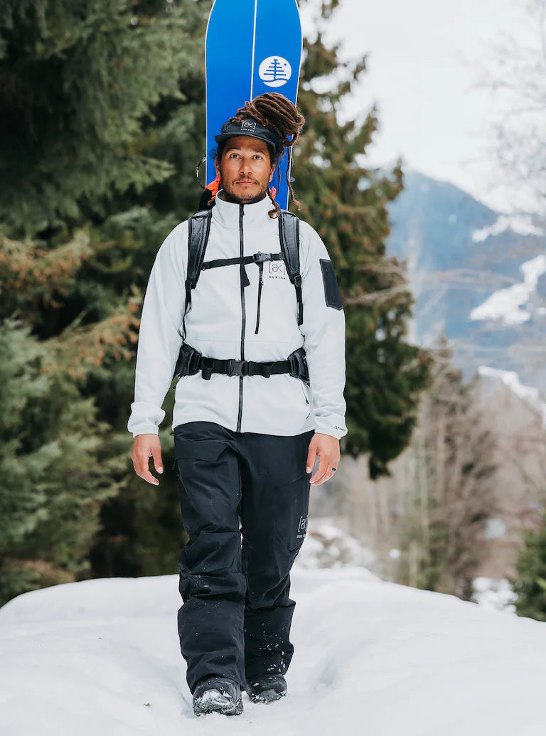 homme pantalon noir veste blanche de ski et snowboard dans le dos lifestyle