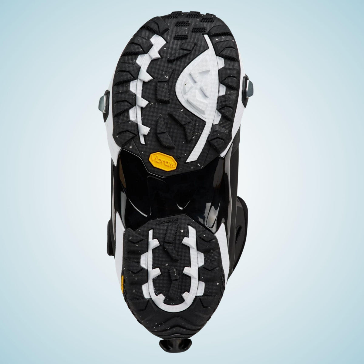 Semelle extérieure vue dessous, avec crampons noirs et blancs, zones de traction profondes et insert jaune au milieu