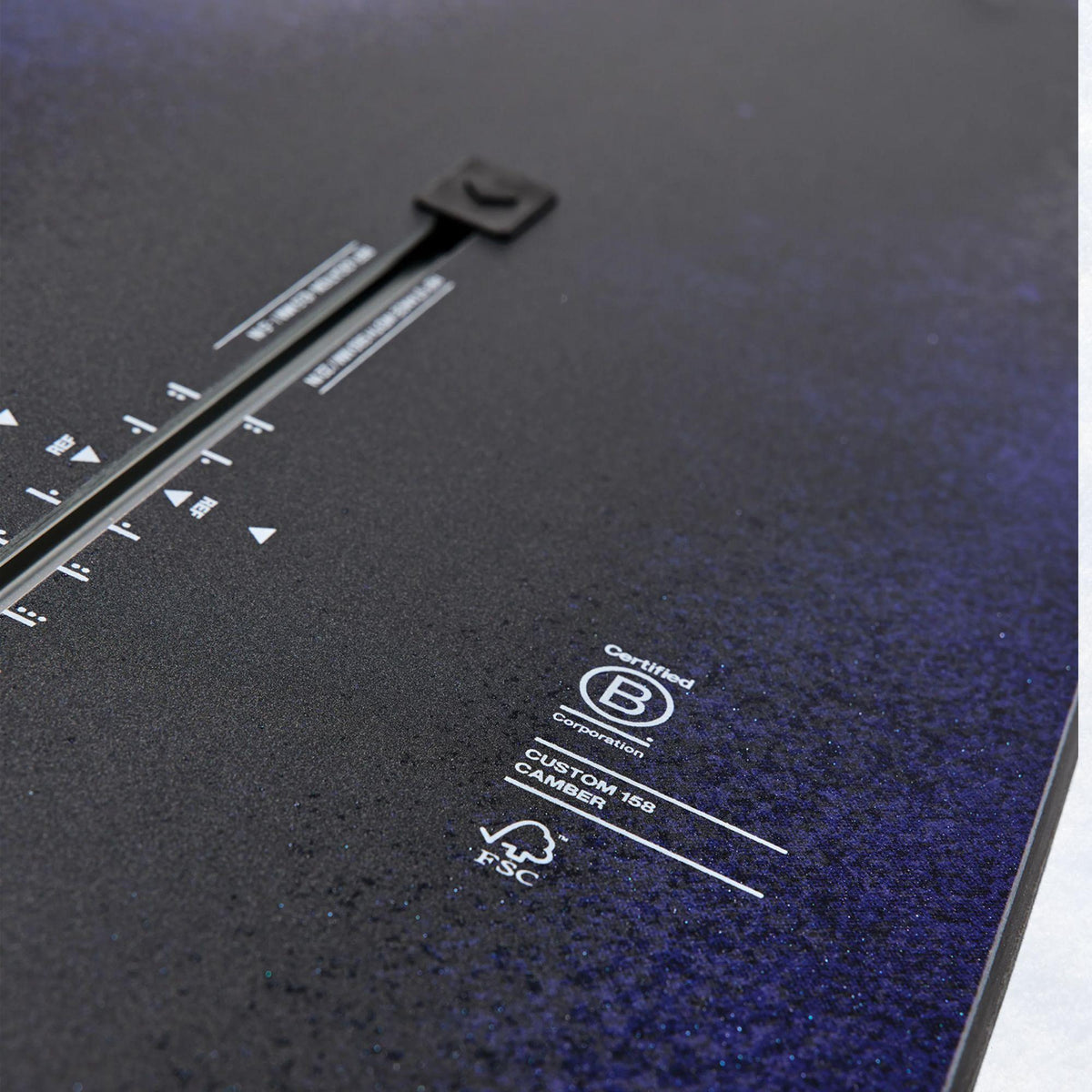 Détail du topsheet sombre texturé, avec repères de stance The Channel et marquages techniques imprimés en blanc