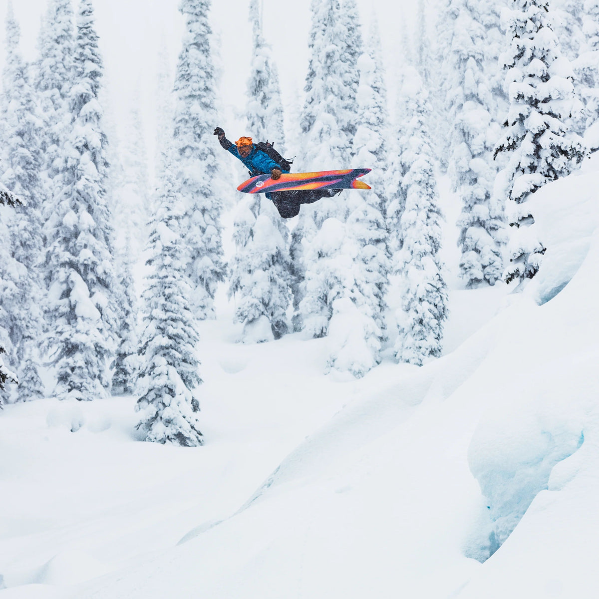 Snowboarder en plein saut dans une forêt enneigée, semelle orange et noire du Burton Smooth Operator visible sous la planche