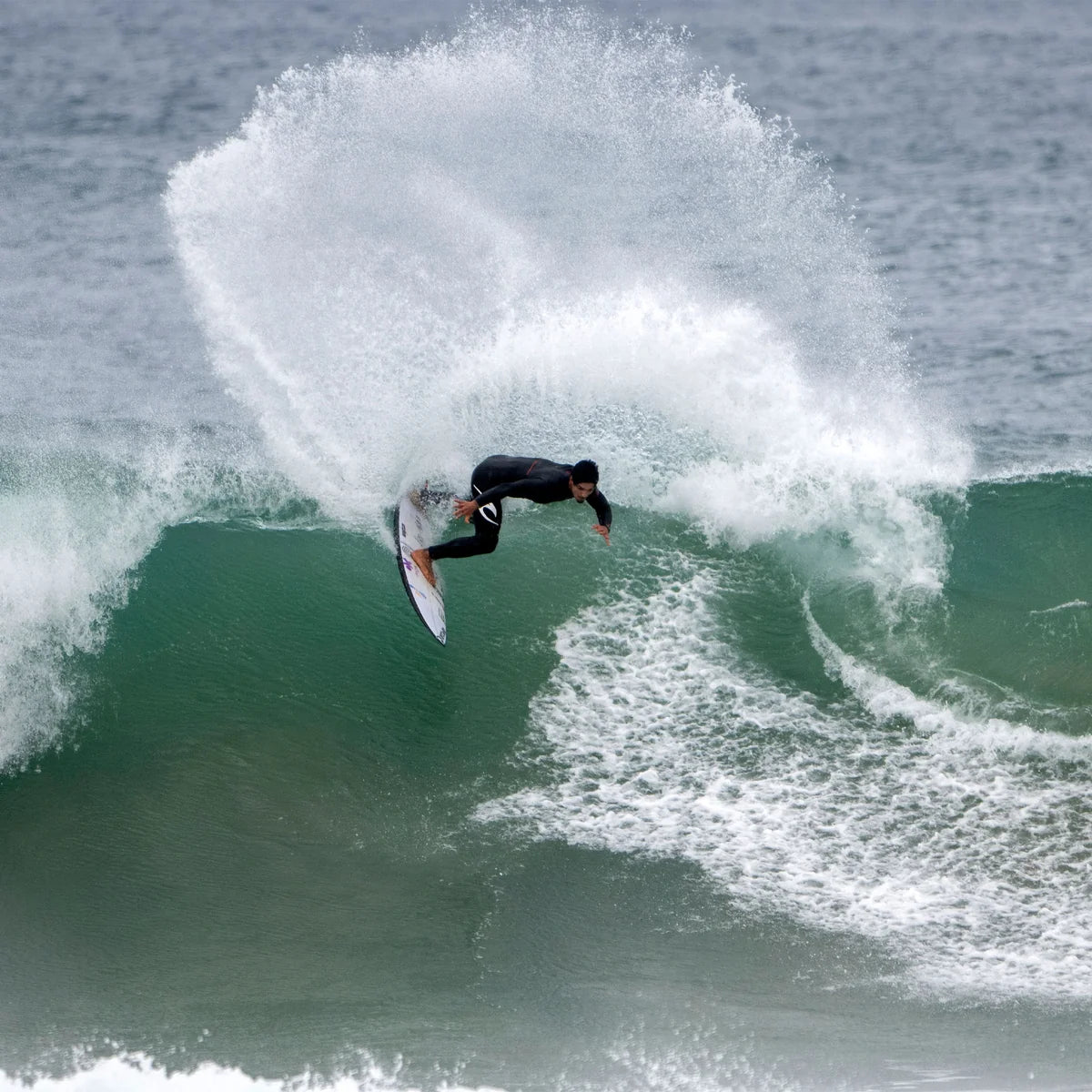Gabriel Medina réalisant une manœuvre sur une vague, avec une grande gerbe d'eau blanche au-dessus de la planche.