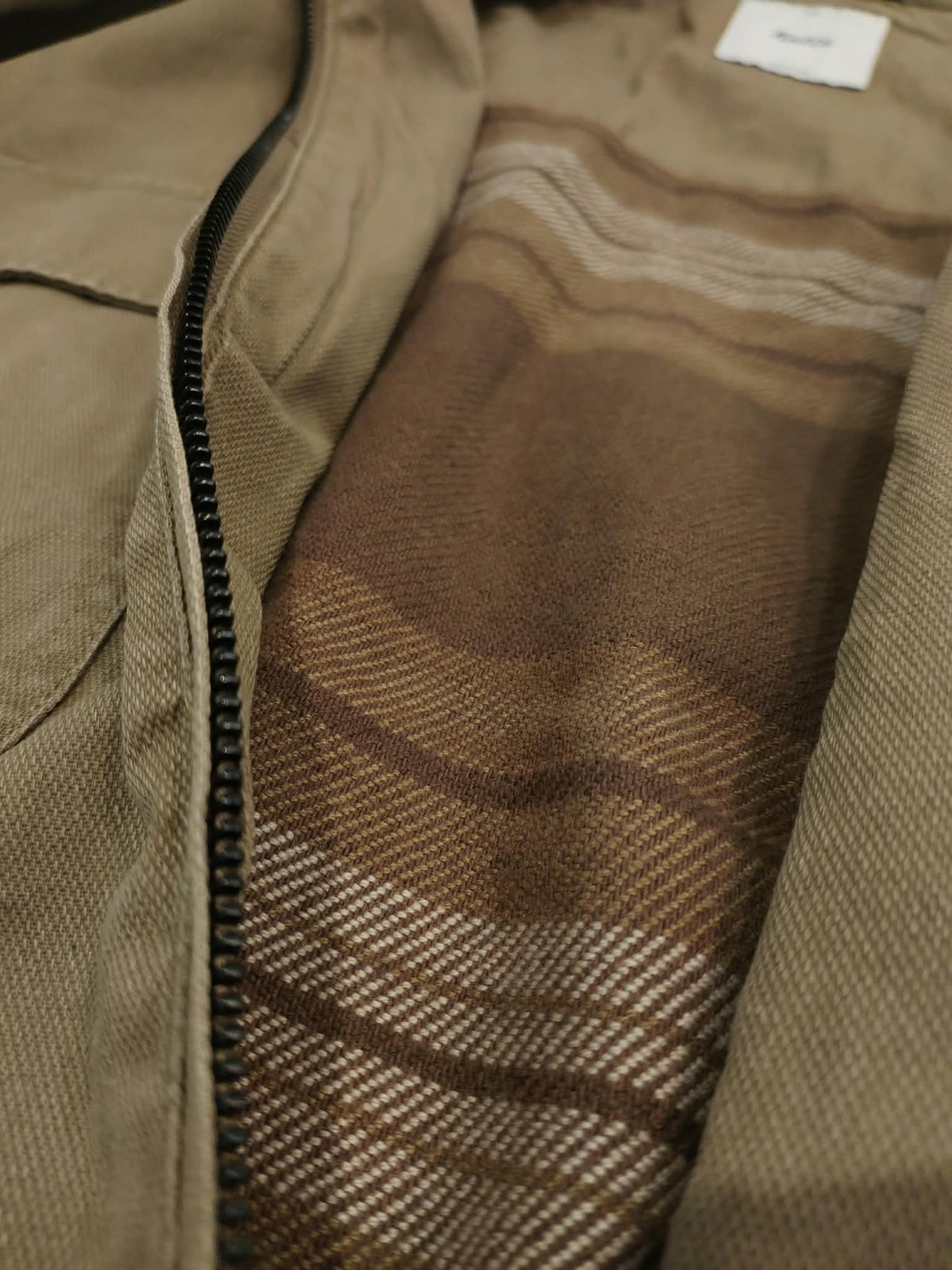 Gros plan sur l'intérieur de la veste Katin Petrol Jacket, doublure en flanelle à carreaux bruns et beiges et fermeture éclair noire.