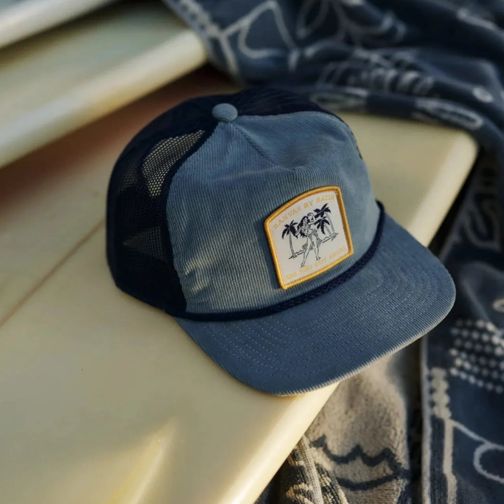 Casquette Katin Aloha Trucker Hat abyss posée sur planche de surf visière courbée filet arrière patch logo frontal