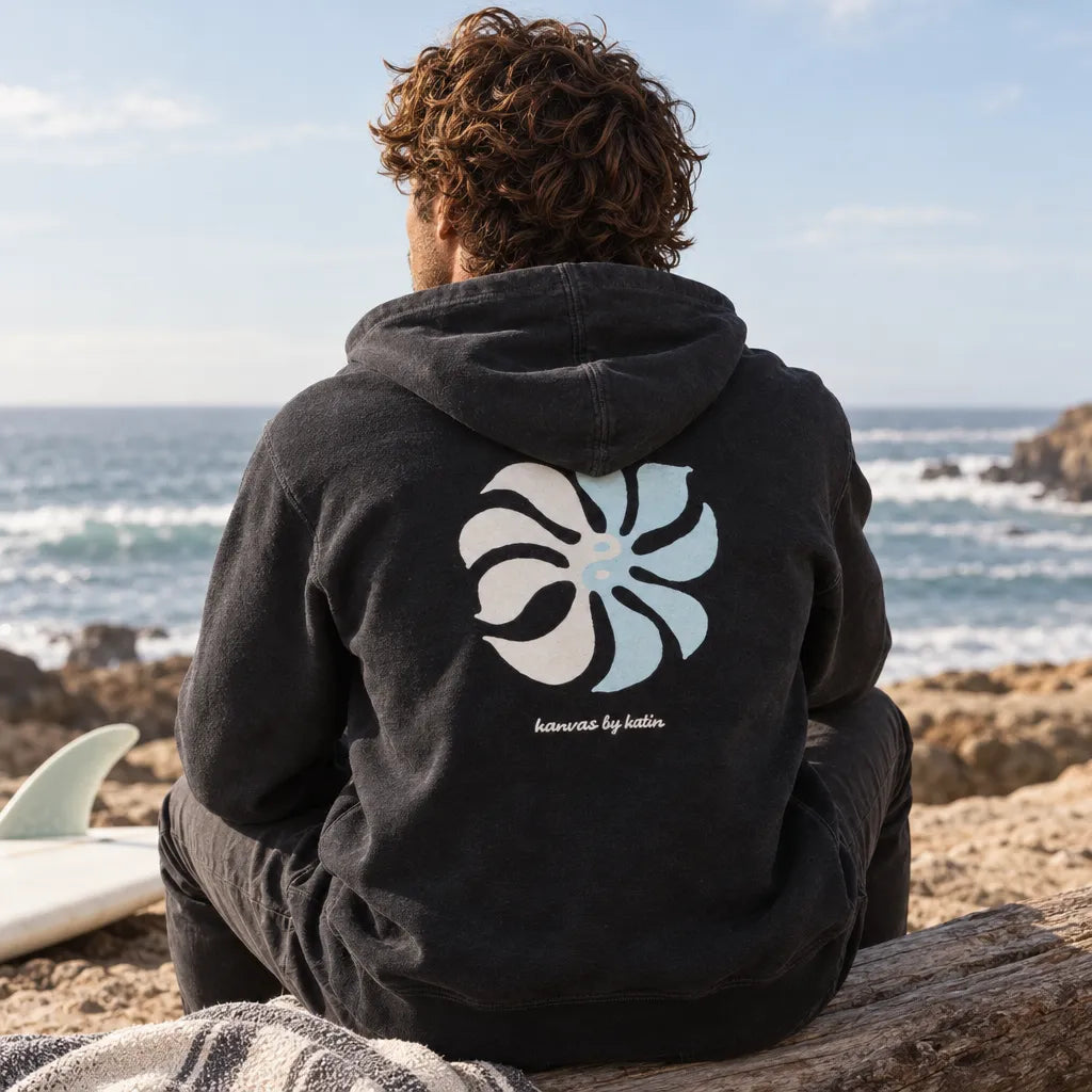 sweat noir homme katin porté assis sur une plage vue de dos avec motif blanc et bleu ciel