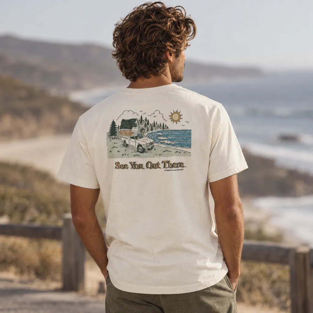 T-shirt Katin Eureka Tee Vintage White blanc écru porté de dos face à l'océan, imprimé paysage vagues, soleil et inscription « See You Out There ».