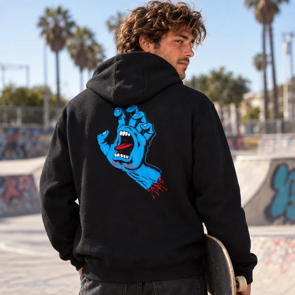 Homme portant un sweat Santa Cruz noir avec grand logo Screaming Hand bleu dans le dos, ambiance skatepark