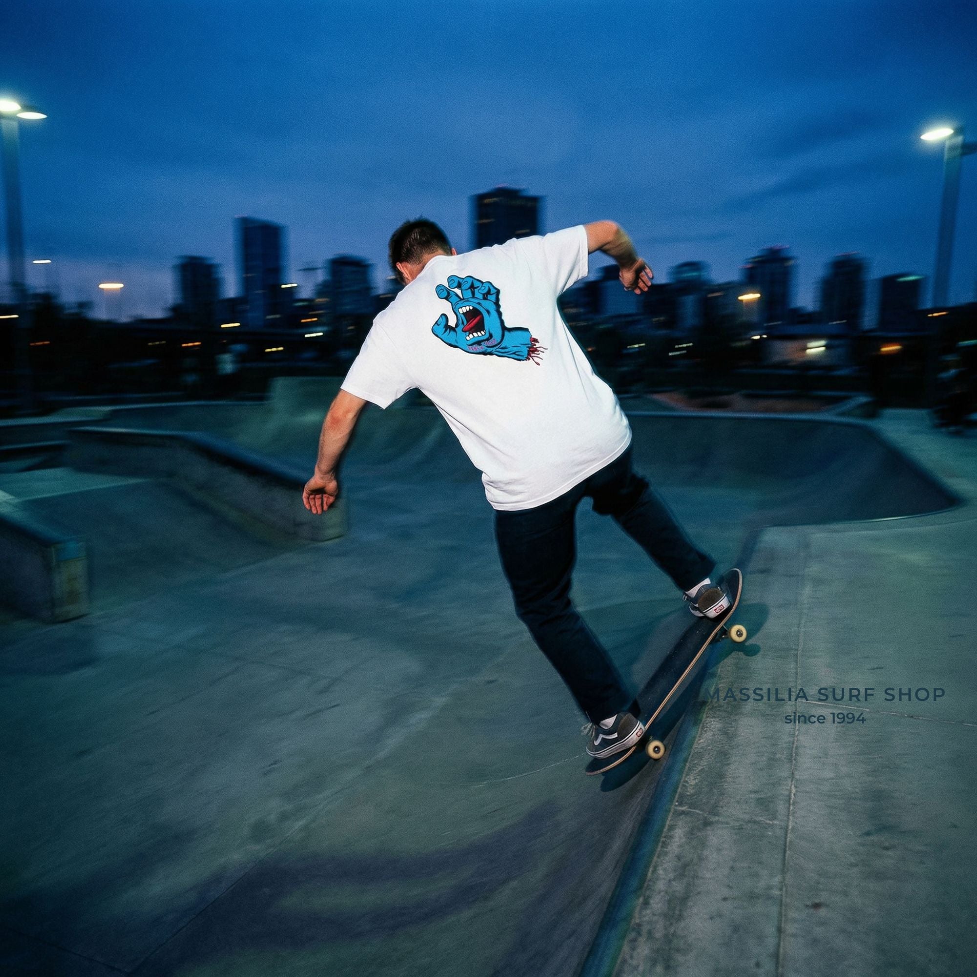 homme en train de faire du skate avec tee shirt blanc et main bleue de santa cruz