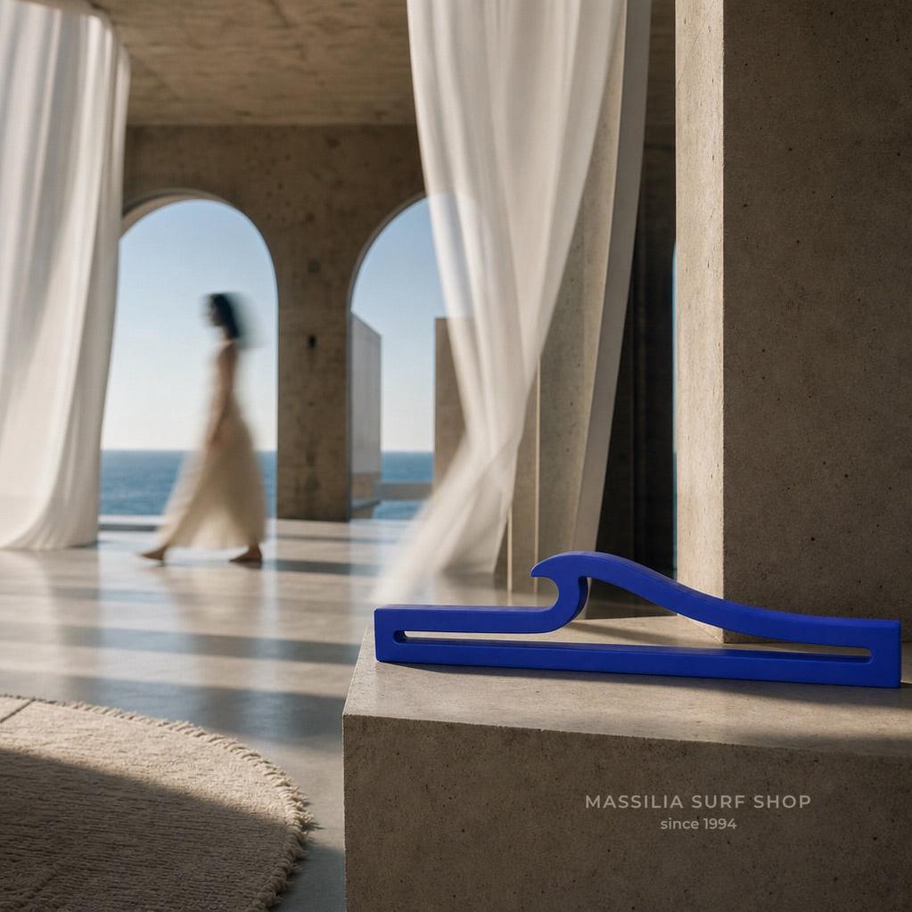 Vague décorative bleue en béton posée sur un socle minéral, dans un intérieur lumineux ouvert sur la mer