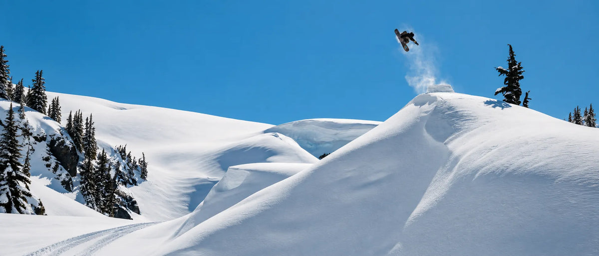 snowboarder en saut avec planche snow burton sur montagne enneigée de poudreuse 