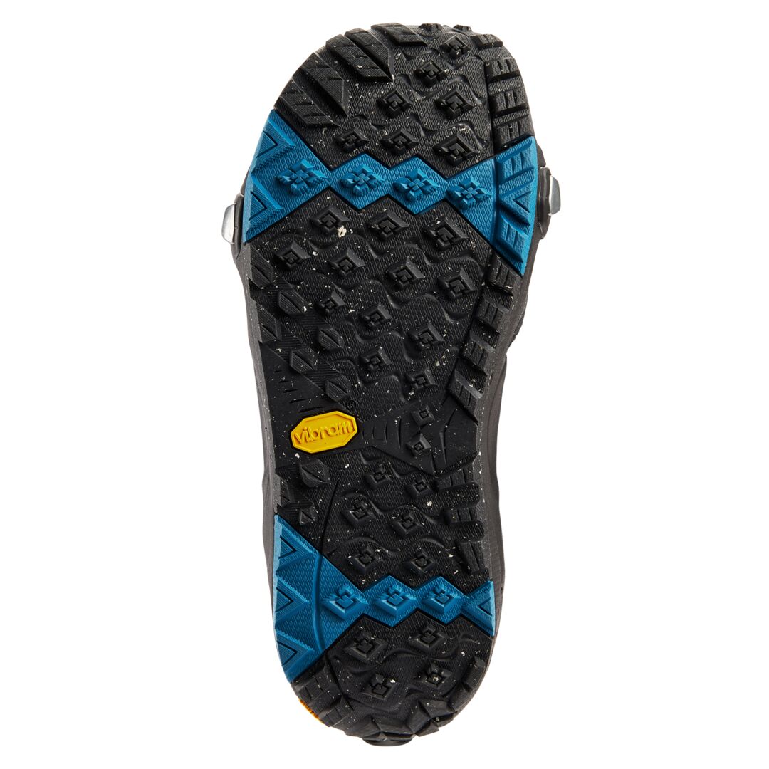 Semelle extérieure noire vue dessous, crampons profonds, zones d’adhérence bleues et insert Vibram jaune au centre
