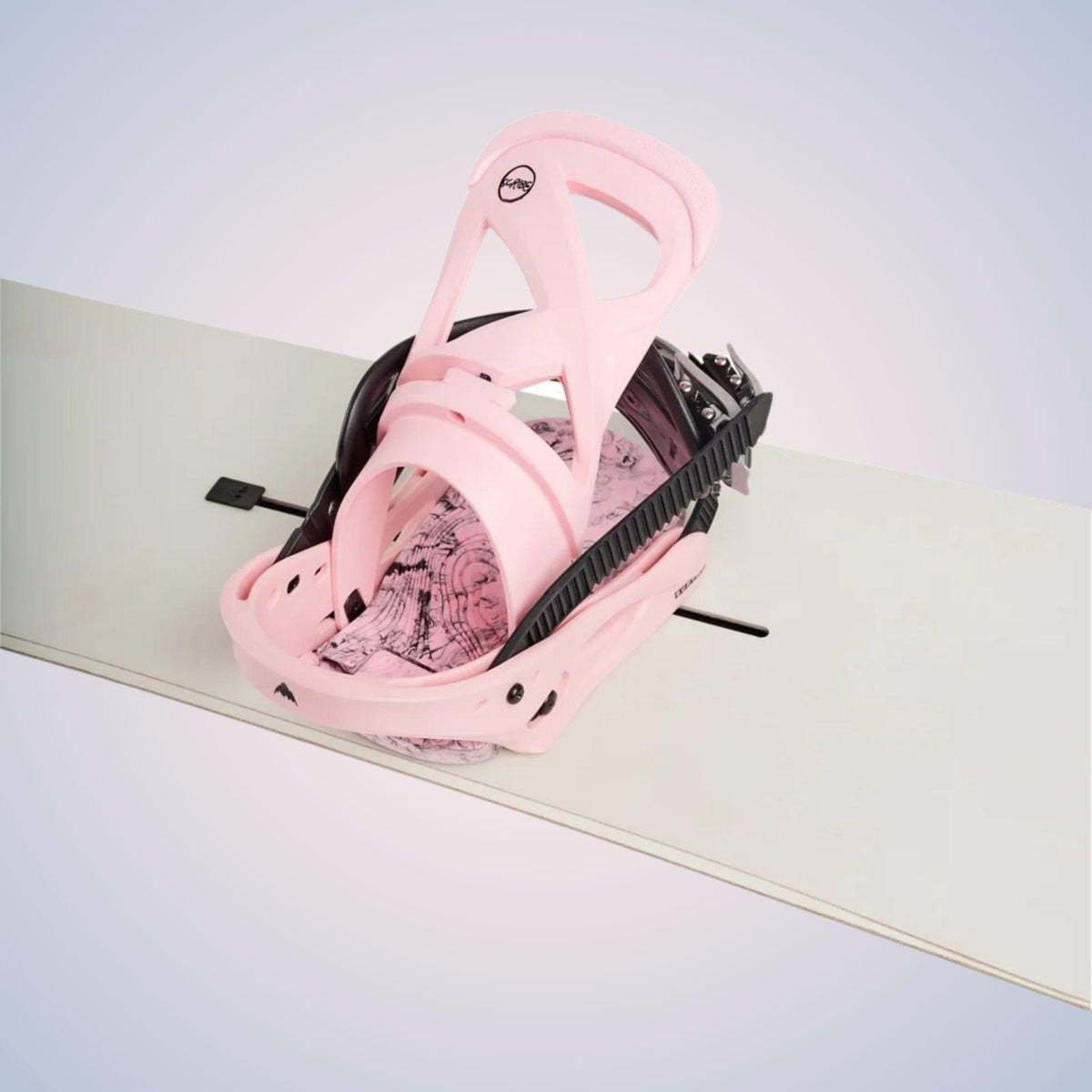 Vue inclinée de la fixation snowboard rose, centrée sur le strap avant, le ratchet, l’embase et les points de réglage monté sur snowboard