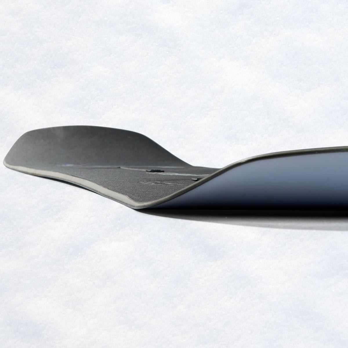 Carre du snowboard vue de profil, révélant la spatule relevée et la superposition des teintes noire, grise et lilas