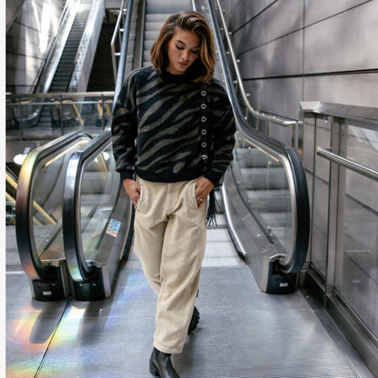 Look féminin avec pantalon Rosalia Veluto beige crème, pull rayé sombre et chaussures noires dans un escalator.