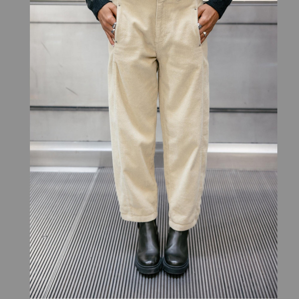 Pantalon Rosalia Veluto porté de face avec les mains dans les poches, jambes légèrement fuselées et chaussures noires.