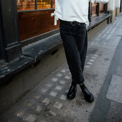 Jean noir vu en marche, coupe raccourcie à revers et tombé souple contrastant avec des chaussures sombres