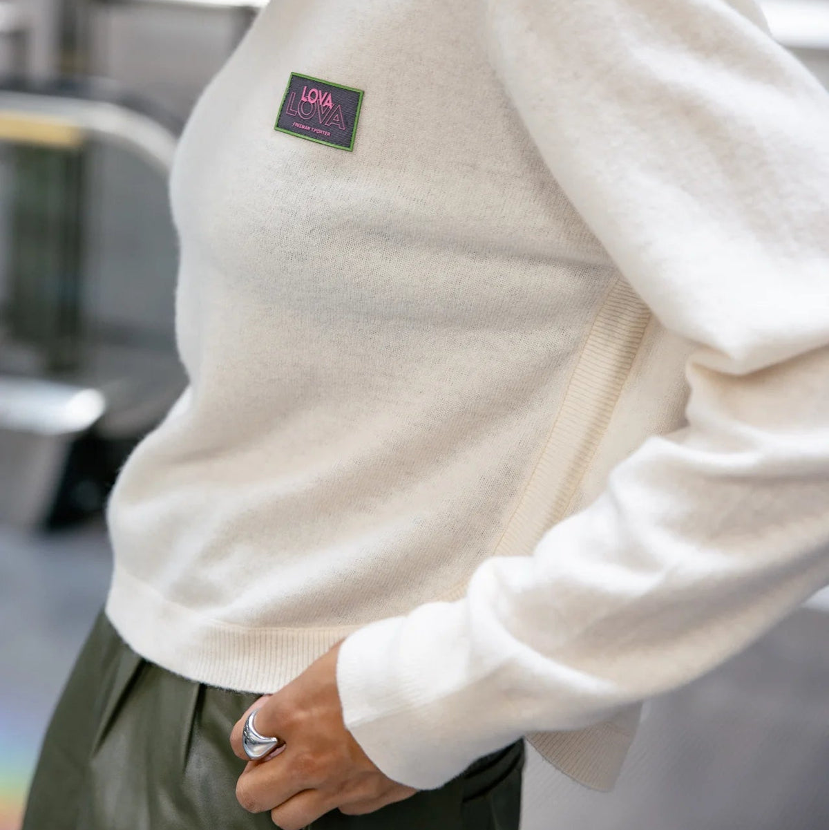Détail du pull écru en maille douce, avec patch poitrine rectangulaire brodé aux nuances rose, vert et foncé