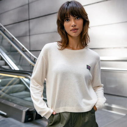Silhouette de face en pull écru à coupe boxy, finitions sobres aux poignets et patch contrastant sur la poitrine