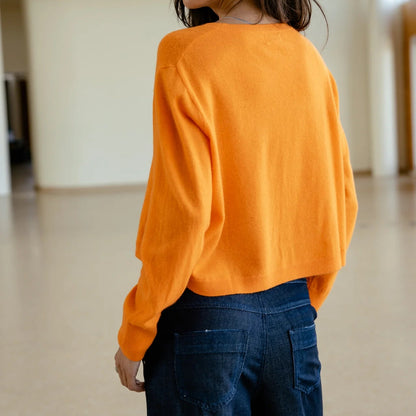 Porté de dos, le pull orange présente une maille unie, un volume ample et une ligne courte à la taille