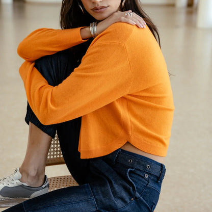 Silhouette assise de profil en pull orange, arrondis en bas, manches généreuses et contraste marqué avec le pantalon bleu
