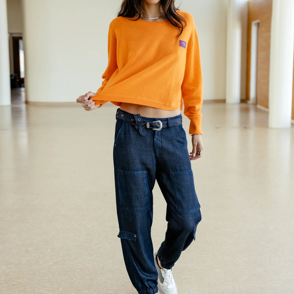 Pull orange porté en mouvement, coupe courte et ample laissant apparaître le tombé droit du bas en maille