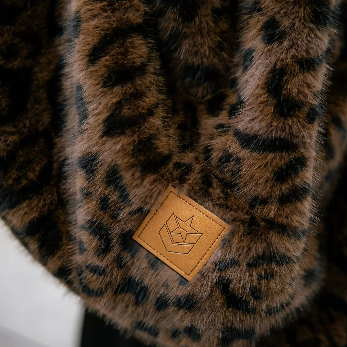 Gros plan sur la fausse fourrure à taches léopard brunes et noires, complétée par un patch carré camel siglé