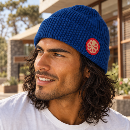 Bonnet surfwear unisexe Jonsen Island Laine bleu porté par un homme, maille côtelée et écusson rond rouge à poulpe doré