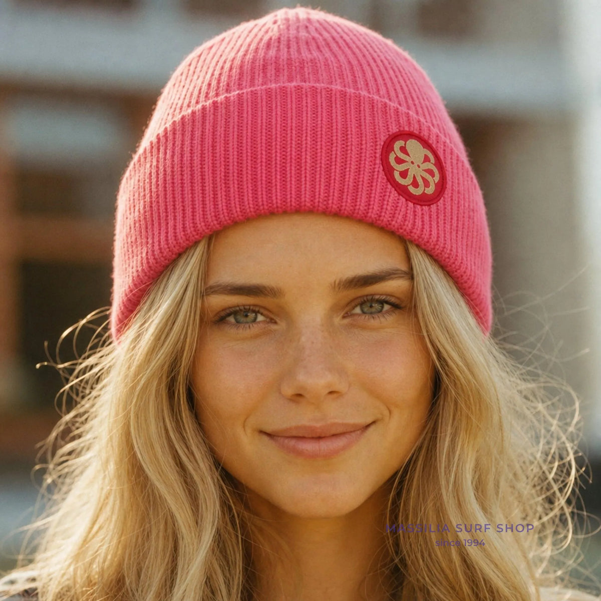 Bonnet surfwear Jonsen Island rose fuchsia porté par une femme, maille côtelée épaisse et écusson rond à pieuvre crème sur le revers