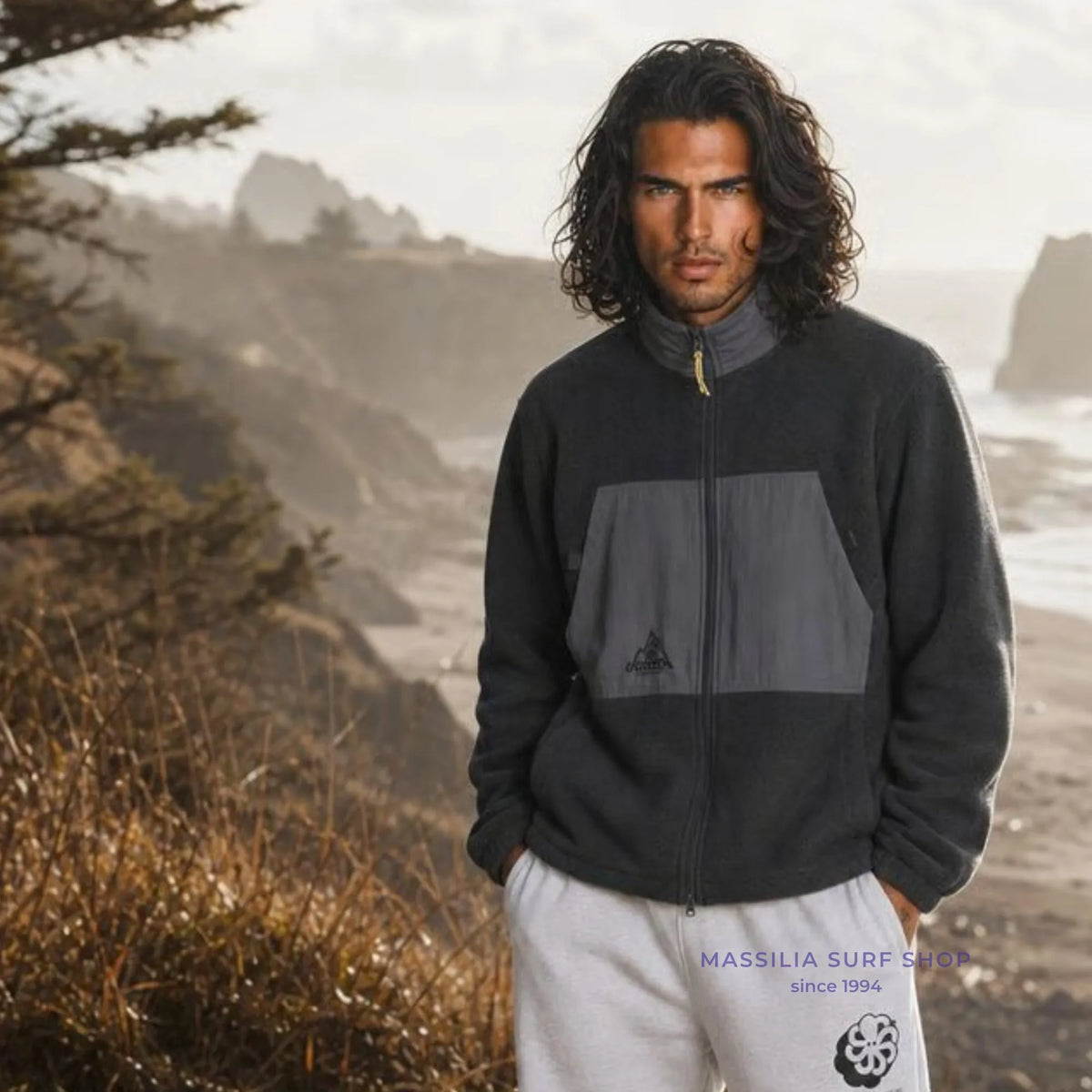 Polaire surfwear Ventura noire portée face à l’océan, col montant, zip intégral et large panneau gris contrastant sur le devant