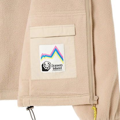 Détail poche du modèle crème, patch montagne multicolore avec pieuvre noire et tirette jaune au bas de la veste