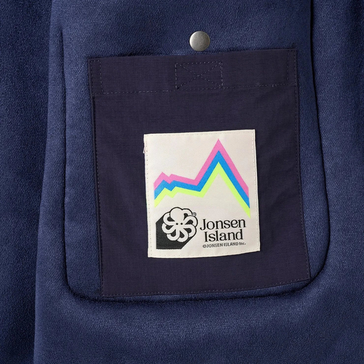 Gros plan sur le patch rectangulaire multicolore cousu sur la poche, avec petit emblème pieuvre et lettrage Jonsen Island