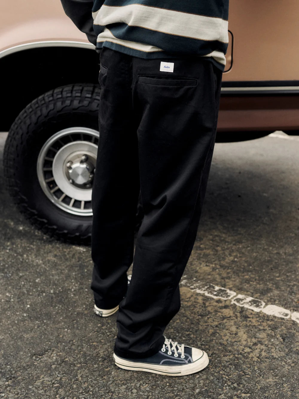 Pantalon Katin Clark noir porté avec baskets, vue rapprochée des jambes et du tombé du tissu devant un véhicule.