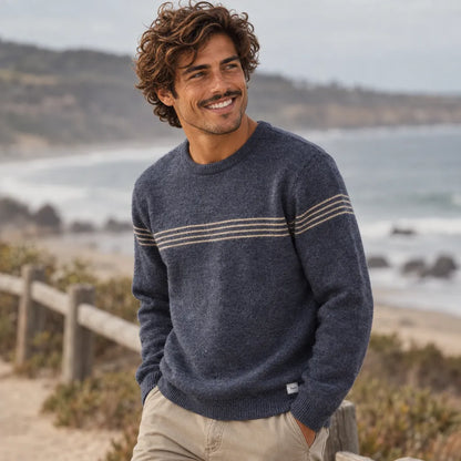 Pull Katin Charles Sweater bleu marine porté de face, col rond, manches longues et fines rayures horizontales claires sur la poitrine, face à l'océan.