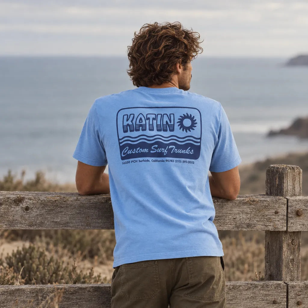 T-shirt Katin Aquatic Blue Wash bleu porté de dos, imprimé Katin Custom Surf Trunks, face à l'océan.