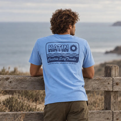 T-shirt Katin Aquatic Blue Wash bleu porté de dos, imprimé Katin Custom Surf Trunks, face à l'océan.