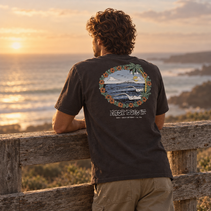 T-shirt Katin Barra Tee Black Wash noir délavé porté de dos face à l'océan au coucher du soleil, grand imprimé circulaire multicolore représentant un paysage côtier.