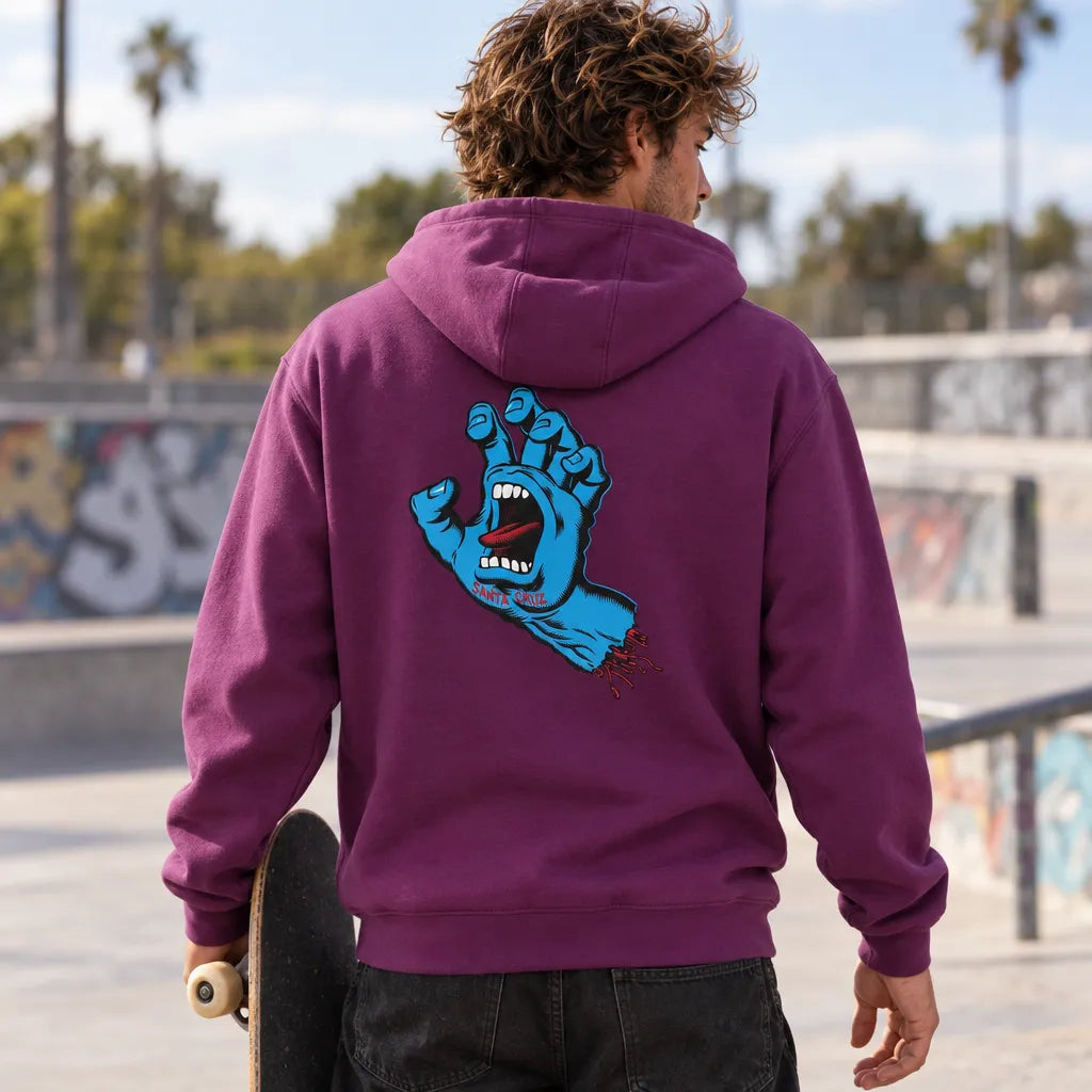 Skateur portant le hoodie Santa Cruz Screaming Hand Fresh Purple, vue de dos au skatepark avec skateboard à la main
