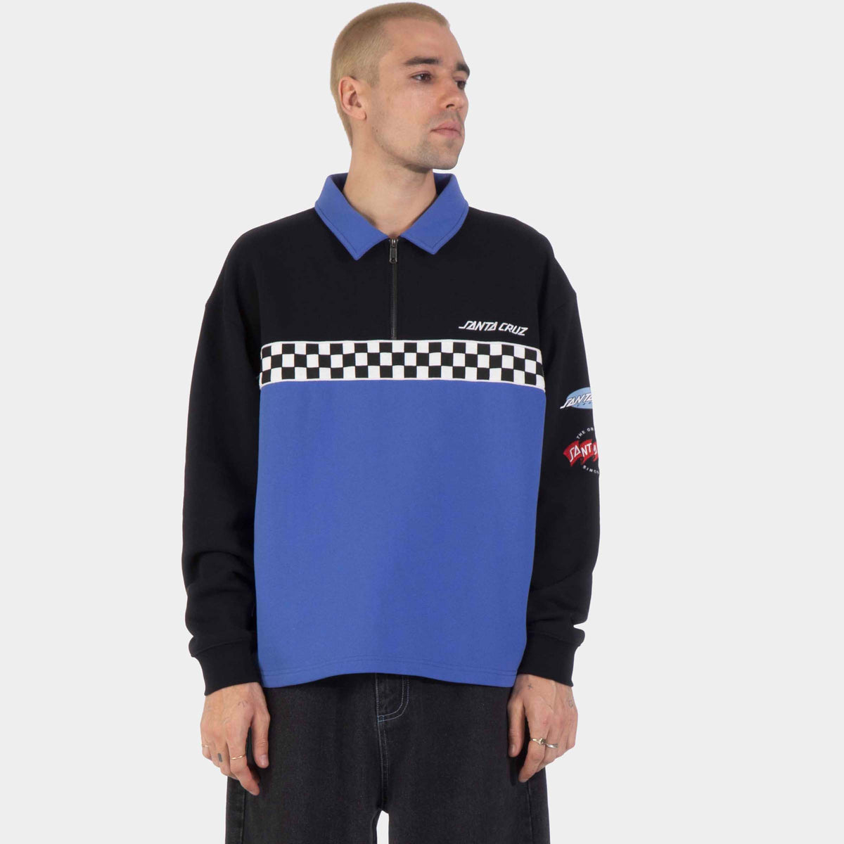 Sweat Santa Cruz Podium 1/4 Zip Crew Black/Sapphire porté de face, col zippé bleu et bande damier noire et blanche sur la poitrine